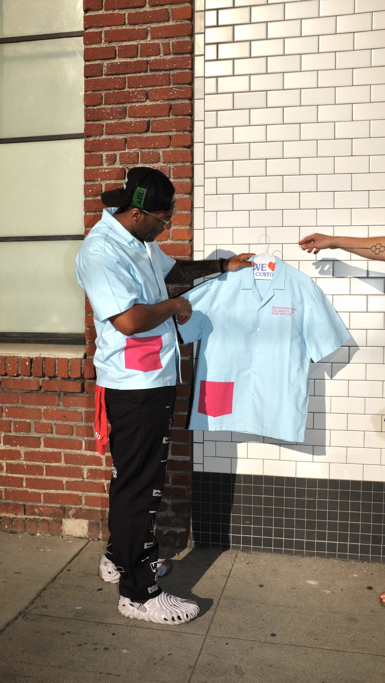Man holding up Rashida Holmes and Bridgetown Roti uniform shirt collaboration designed by Finery.